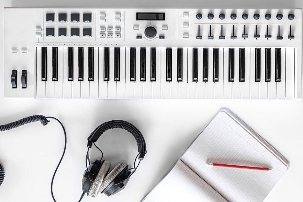桌上擺著一架白色的鋼琴、耳機及筆記本，思考透過音樂的剪輯軟體製作音檔