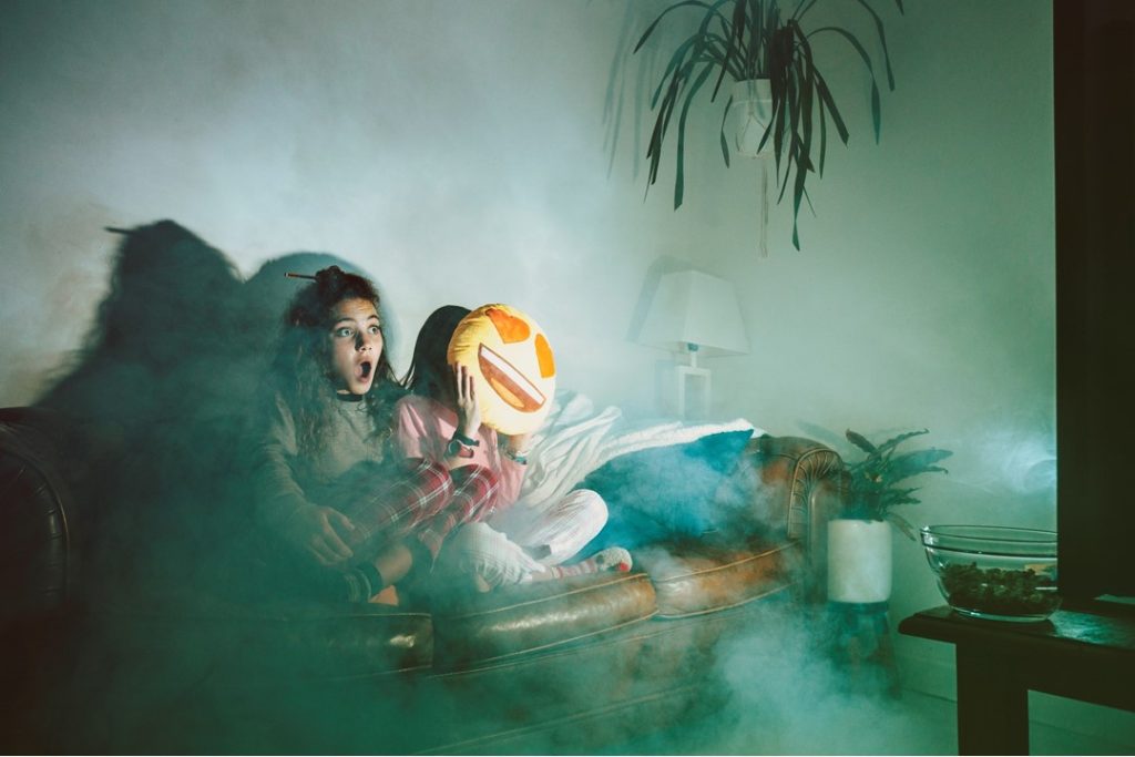 兩個女孩坐在客廳沙發上，看著電視張大嘴感到害怕，中元普渡總是讓人又愛又怕