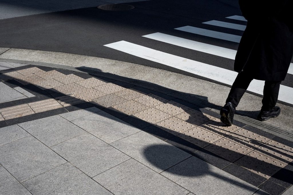 一個人穿著黑色大衣，準備走向斑馬線過對面馬路，斑馬線彷若行人地獄，讓人感到躊躇