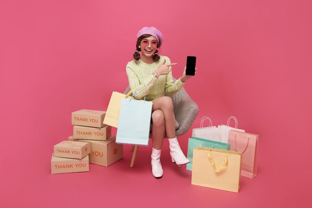 一個女生坐在沙發上用手機，旁邊都是購買的包裹與紙袋，即便是飄洋過海購物，用手機也很方便